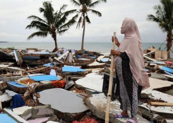 Seorang perempuan melihat desanya di Indonesia yang hancur akibat tsunami. (Foto: ©️ OCHA/Anthony Burke)