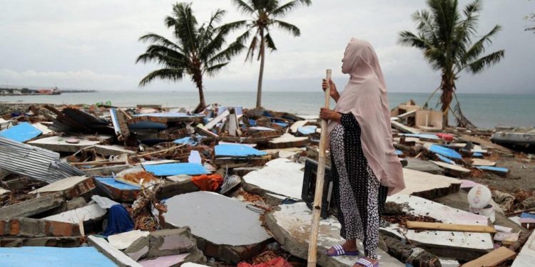 Seorang perempuan melihat desanya di Indonesia yang hancur akibat tsunami. (Foto: ©️ OCHA/Anthony Burke)